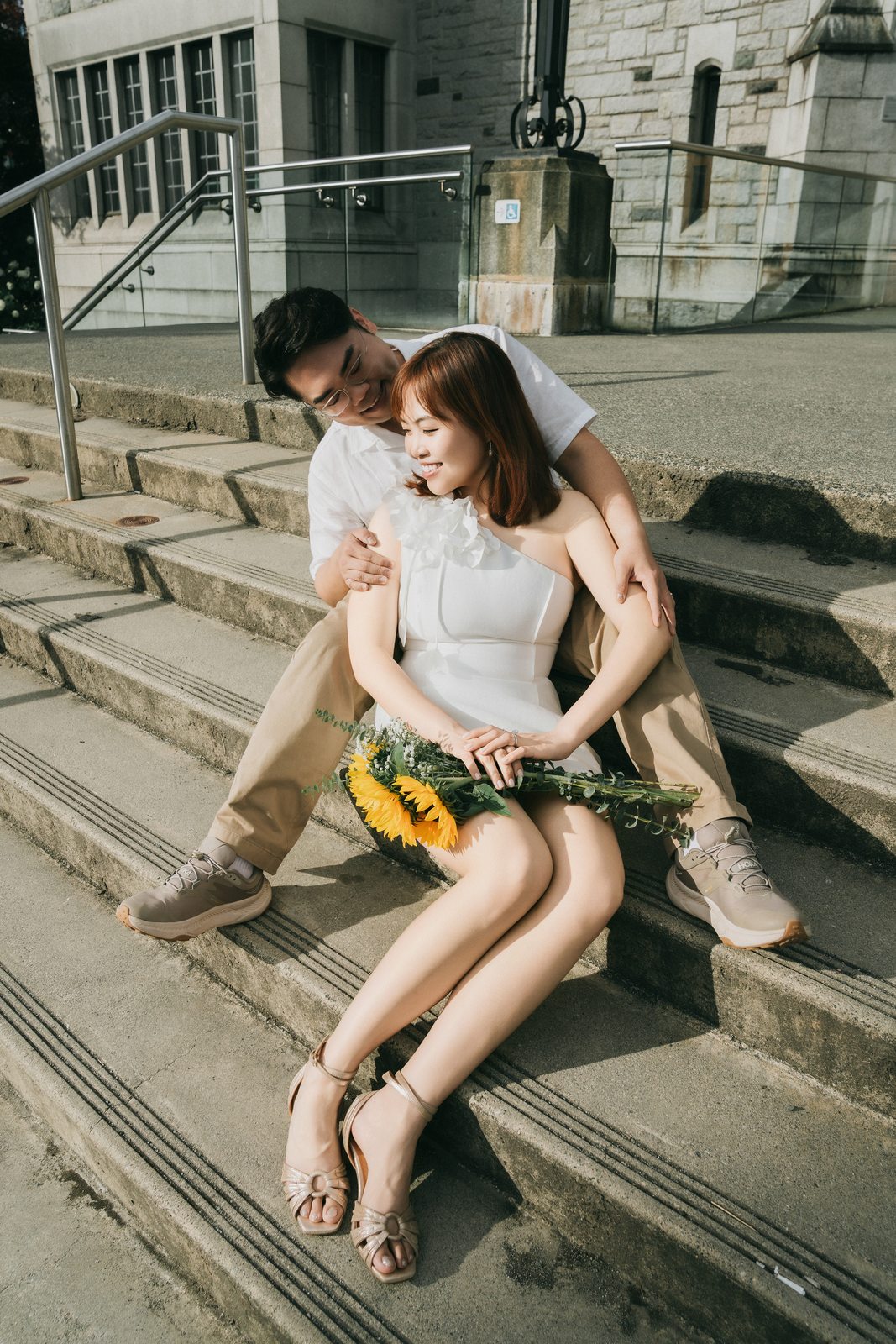 Richard and Mabel sitting close together on wide stone steps with a sunflower bouquet