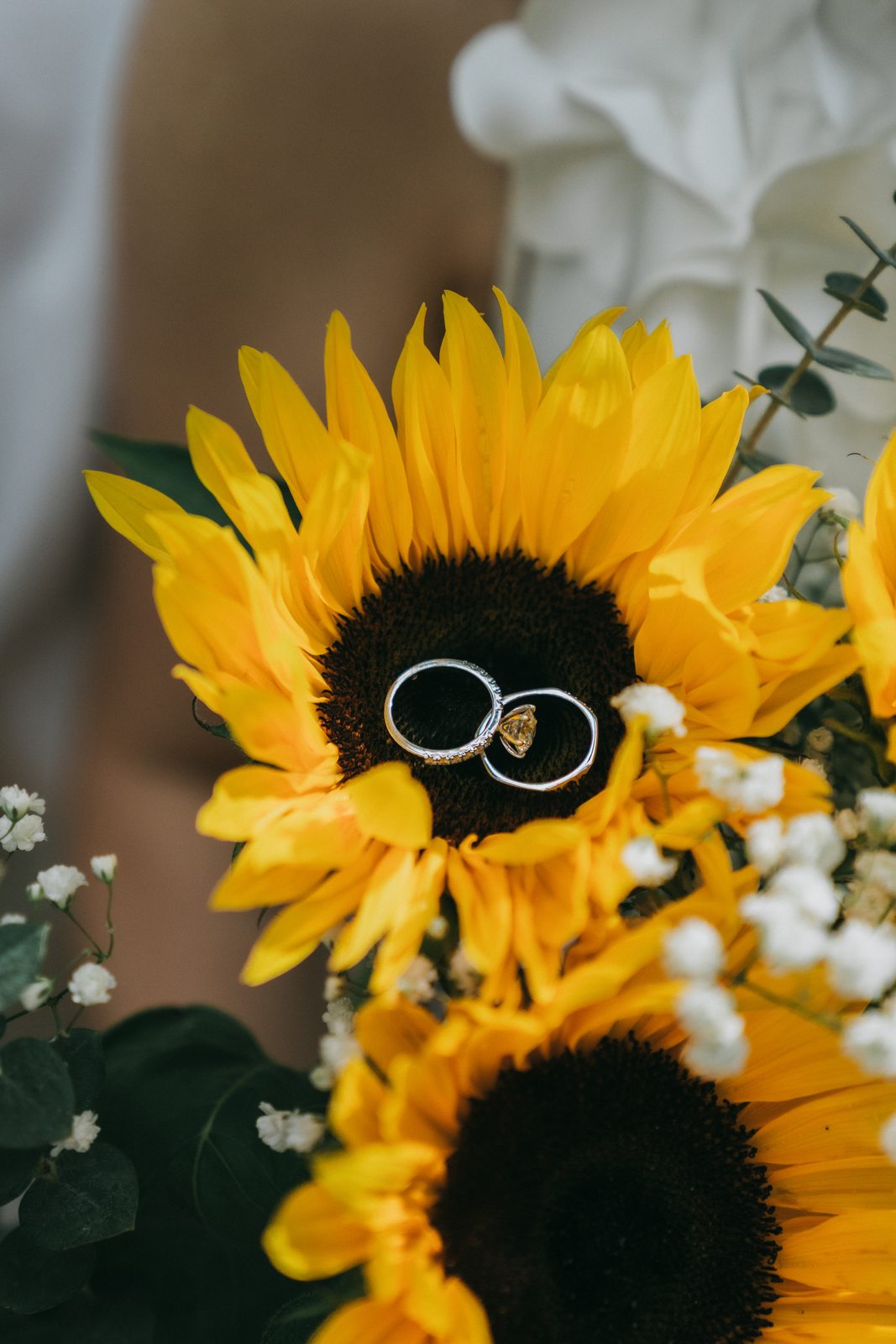 Two wedding rings resting on the face of a sunflower in the bridal bouquet