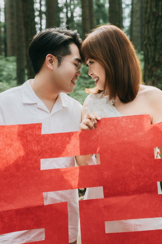 Richard and Mabel smiling forehead to forehead behind large red double-happiness paper cutouts