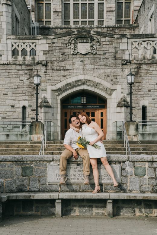 Richard and Mabel laughing together on a stone ledge outside a UBC building