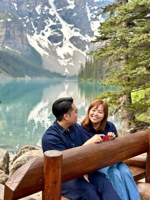 Richard and Mabel on a wooden bench at Moraine Lake holding two red double-happiness characters